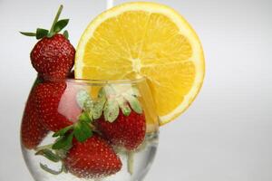 un vaso de agua con fresas y un naranja rebanada foto