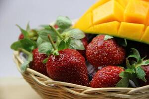 a basket of strawberries and mangoes on the cutting board on white background photo