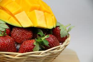 un cesta de fresas y mangos en el corte tablero en blanco antecedentes foto