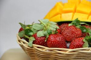 un cesta de fresas y mangos en el corte tablero en blanco antecedentes foto