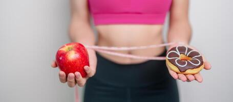 woman hand hold red Apple and donut, female fitness choose between fruit is Healthy and sweet is Unhealthy junk food. Dieting control, Weight loss, Obesity, eating lifestyle and nutrition concept photo