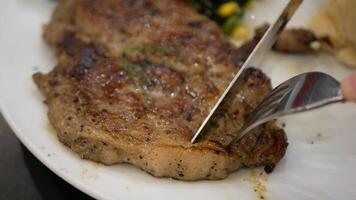 close up to a plate of pork meat american steak style while using knife and fork to cut to eat steak for dinner meal video