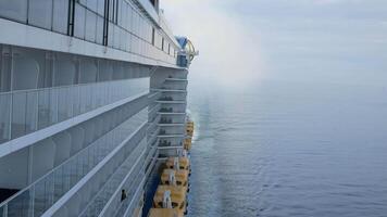 view to the back aft of the cruise ship from front deck area with side view of the passenger cruise ship while cruising in the sea in day time with many lifeboats video