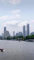 vertical lapso de tiempo panorama paisaje ver de chaopraya río con río agua barco transporte y antecedentes de Bangkok ciudad horizonte con muchos Alto rascacielos entre central distrito zona video