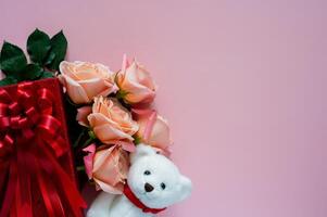Pink roses in red gift box with white teddy bear doll on pink background for Valentines day concept. photo