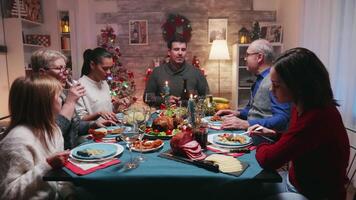 Versammlung von groß Familie um das Tabelle mit köstlich Essen zu feiern Weihnachten. traditionell festlich Weihnachten Abendessen im Mehrgenerationenhaus Familie. genießen Weihnachten Mahlzeit Fest im dekoriert Zimmer. groß Familie Wiedervereinigung video
