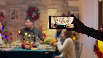 Girl taking a family portrait with her phones while celebrating christmas. Traditional festive christmas dinner in multigenerational family. Enjoying xmas meal feast in decorated room. Big family reunion video