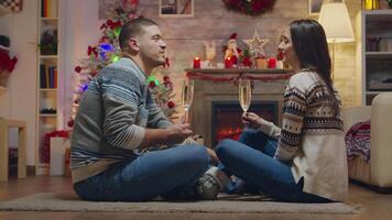 couple tintement une verre de Champagne séance sur le tapis dans de face de cheminée célébrer Noël. video