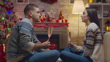 Couple having a conversation and drinking champagne while celebrating christmas in front of fireplace. video