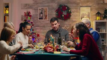 Big family waving during a video call at christmas reunion. Christmas tradition. Traditional festive christmas dinner in multigenerational family. Enjoying xmas meal feast in decorated room. Big family reunion