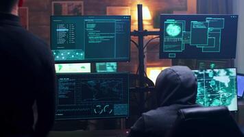 Back view of hooded cyber terrorist using super computer in dark room. Team of hackers. video