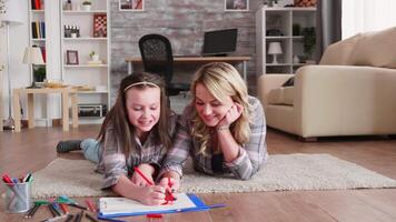 Little girl with braces and her mother sitting on floor carpet drawing. video