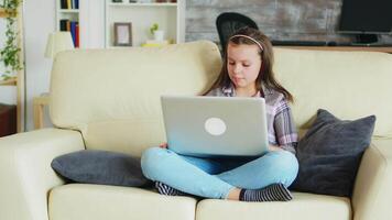 Sweet little girl with braces sitting on the couch using her laptop. Happy kid. video