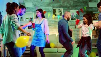 Bald attractive young man smiling while dancing at the party with his friends. Wild college party with neon lights and disco ball video