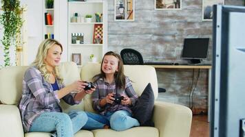 Mother and daughter playing video games using wireless controller sitting on the couch.