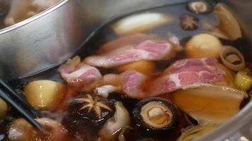 Close up of people eating together using Chopsticks putting vegetable and meat into the hotpot red spicy boiling Chinese Sichuan style soup video