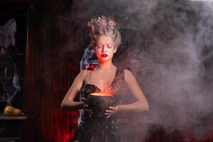 Halloween Witch with cauldron. Beautiful young woman conjuring, making witchcraft photo