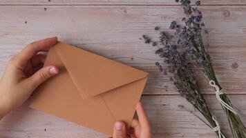 Female hands taking paper card note with text MAKE YOURSELF A PRIORITY from beige envelope. Lavender flower. Top view, flat lay. Concept of mental spiritual health self care wellbeing mindfulness video