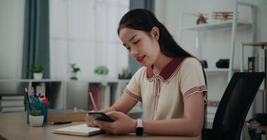 Footage dolly shot, Selective focus,Happy young asian woman sitting at desk writing noting information to diary from smartphone at home, creative thoughts to journaling, idea and inspiration video