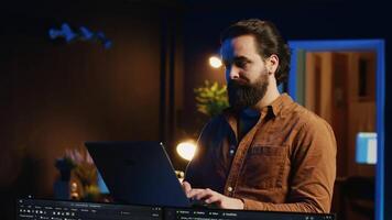 Portrait of smiling man doing IT support job from home, standing in personal office with laptop in hand, coding. Cheerful programmer writing lines of code on notebook in living room, camera A video