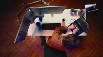 Top down view of hyperactive developer suffering from adhd, writing code, drinking coffee, listening music, arranging desk objects. Distracted IT admin doing multitasking in home office, aerial shot video