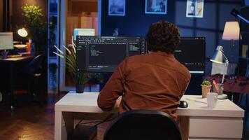 Computer scientist at home office desk writes binary code scripts and drinks from mug of coffee. IT expert in apartment enjoying tea while using programming to safeguard consumer data, camera B video