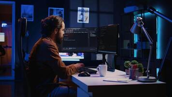 Programmer doing web development during remote job shift in neon lit home office, finishing coding project. IT specialist sitting at computer desk, working on desktop PC, camera B video