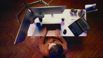 Top down view of self employed man doing IT support job from apartment personal office, coding on PC, drinking coffee. Software developer writing lines of code on computer at home, aerial shot video