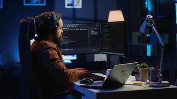 Engineer typing code in apartment office, using javascript programming language to develop software application. It admin using multimonitor desktop setup and notebook to finish tasks, camera A video