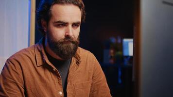 Software technician in apartment office deeply immersed in coding on computer at desk, close up. IT freelancer absorbed by work, focused on screen, writing lines of code at workstation, camera B video