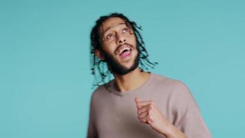 Happy middle eastern dancer having fun, dancing on rhythm, enjoying leisure time. Cheerful BIPOC man entertaining himself doing funky movements on music, studio background, camera B close up video