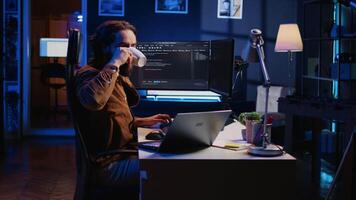 Developer writing lines of code on multimonitor PC setup during remote job shift. IT expert doing multitasking in neon lit home office, listening music, drinking coffee, camera B video