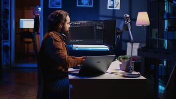 Technician typing code in neon lit personal office, using javascript programming language to develop software application. It specialist using multimonitor desktop setup to finish project, camera B video