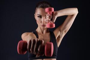 athletic girl in white clothes with dumbbells, on a dark background photo