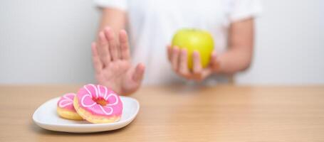 woman hand hold green Apple and reject donut, female fitness choose between fruit is Healthy and sweet is Unhealthy junk food. Dieting control, Weight loss, Obesity, eating lifestyle and nutrition photo