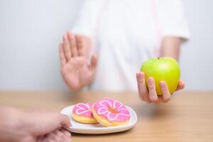 woman hand hold green Apple and reject donut, female fitness choose between fruit is Healthy and sweet is Unhealthy junk food. Dieting control, Weight loss, Obesity, eating lifestyle and nutrition photo