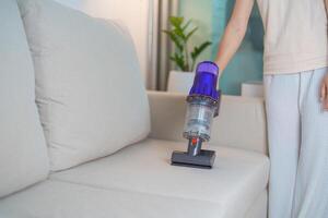 Woman cleaning Sofa with cordless Vacuum cleaner. Housewife using wireless Hoover for big cleaning home. Housework, Housecleaning, Housekeeping, Removes dust, Domestic hygiene and daily routine photo