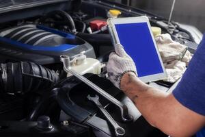 The mechanic checks the engine using tablet computer technology. Complete with wrench tool Auto mechanic working in the garage. Repair service. photo