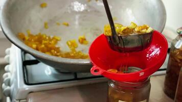 woman hands filling glass jars with apple jam via red funnel and soup ladle, slow motion closeup video