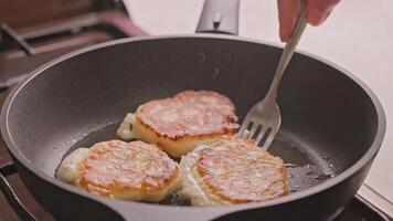 hand with fork flipping domestic pancakes roasting on cast iron pan covered with vegetable oil video