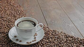 black coffee in a cup with spinning bubbles on a wooden surface partially covered with coffee beans video