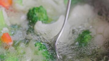 spoon stirring and removing scum foam out from boiling broccoli, cauliflower and red bell pepper video