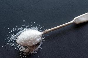 Spoon with white sugar on the dark background photo