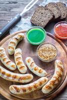Grilled sausages with hot sauces on the wooden board photo