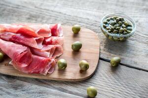 jamón con alcaparras y aceitunas sobre la plancha de madera foto