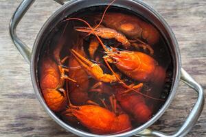 Pot with boiled crayfish on the wooden table photo