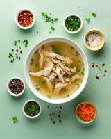 AI generated Chicken soup in a white bowl with small bowls of ingredients around it on a light green top table photo