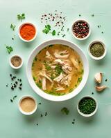 AI generated Chicken soup in a white bowl with small bowls of ingredients around it on a light green top table photo