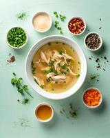 AI generated Chicken soup in a white bowl with small bowls of ingredients around it on a light green top table photo