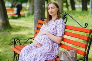 The young pregnant woman has a rest on a bench in park photo
